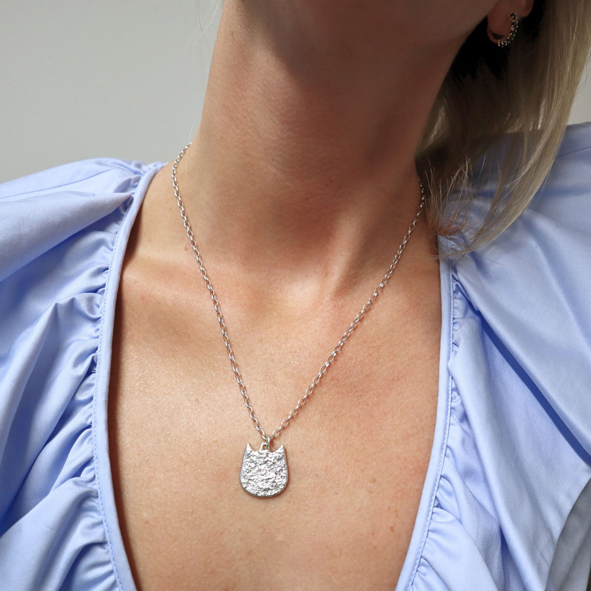 Bee wearing a silver necklace with a cat-shaped pendant against a light background